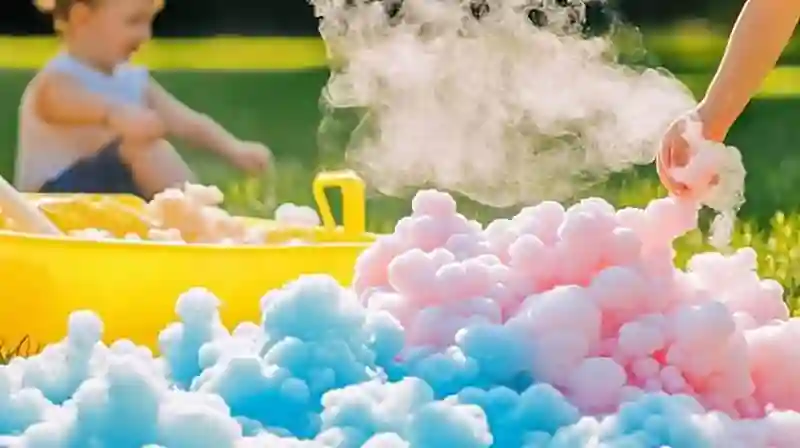 Hand and Child in Colorful Foam Sensory Play A hand reaching into colorful blue and pink foam outdoors, with a child in the background playing near a yellow bin.