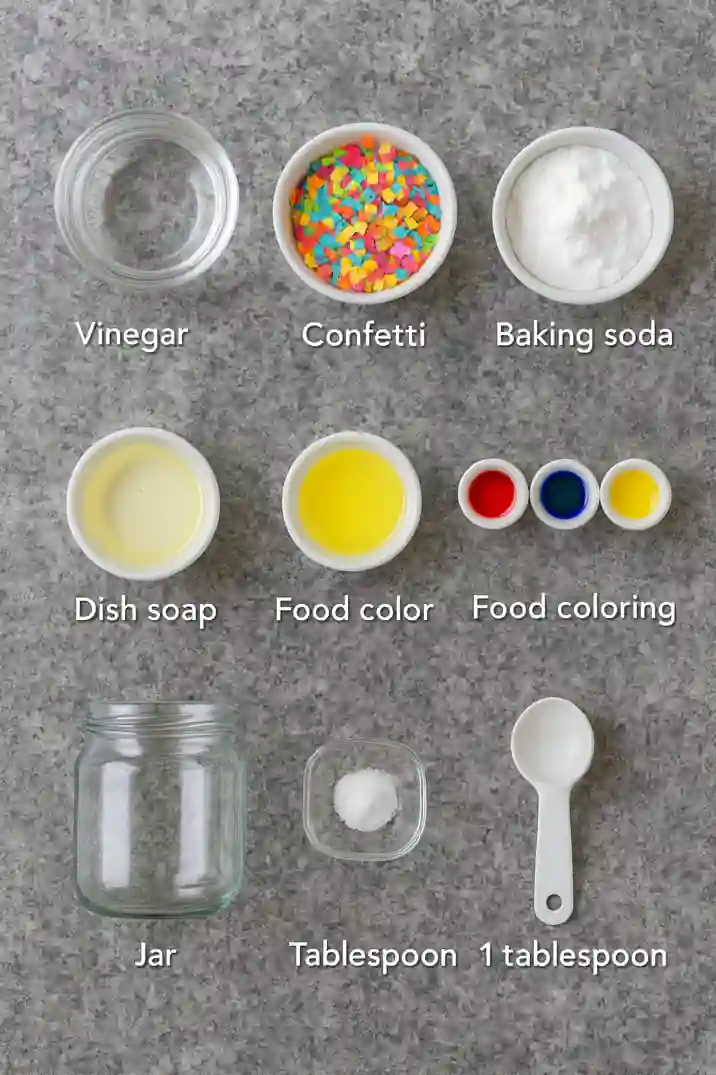 confetti-jar-explosion-experiment-ingredients Vinegar, baking soda, dish soap, food coloring, and confetti arranged on a gray surface