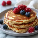 Fluffy Flourless Cottage Cheese Pancakes: High Protein & Naturally Delicious 3 Stack of golden pancakes topped with raspberries and blueberries on a plate